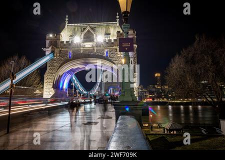 Una lunga esposizione notturna scattata sul Tower Bridge con un pedone, i turisti che visitano questo iconico monumento e i sentieri luminosi dai veicoli di passaggio. Foto Stock