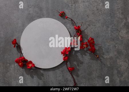 Podio bianco per la presentazione del prodotto con fiori rossi su sfondo grigio. Piattaforma cilindrica vuota per cosmetica. Mockup con cerchio in cemento e cod Foto Stock