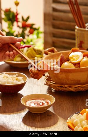 Vista frontale della mano che tiene un pezzo di uovo brasato su un tavolo di legno. Vassoio Tet Cibo tradizionale nel capodanno lunare. Foto Stock