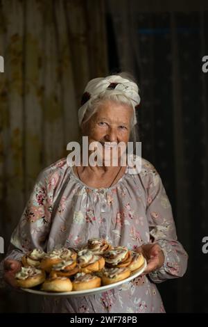 La nonna, vecchia e felice, cucina in cucina, impasti l'impasto e prepara i biscotti Foto Stock