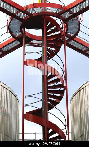 Scala a chiocciola rossa e piattaforma di ispezione sopra le vasche di stoccaggio, birreria Carlsberg, Northampton, Regno Unito Foto Stock