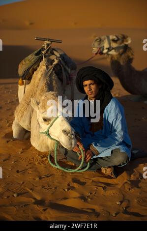 Una guida cammello siede con il suo animale tra le dune di sabbia all'alba. Foto Stock