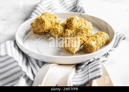 Primo piano del baklava arrotolato su un piatto bianco di marmo Foto Stock