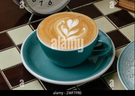 caffè in una tazza sul tavolo. gli orologi e i libri sono vicini Foto Stock