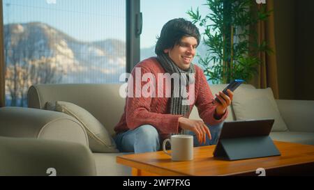 Uomo seduto sul divano navigando in Internet sul telefono cellulare, controllando e-mail, leggendo notizie sui media, scorrendo i social network, utilizzando applicazioni mobili su smartpho Foto Stock