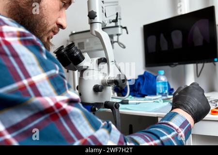 Il dentista maschile utilizza il microscopio dentale nel trattamento dei denti. Il medico di stomatologia esamina le immagini dei denti sul monitor del microscopio. Attrezzature odontoiatriche high-tech. Foto Stock