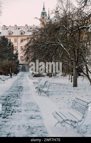 Parco innevato a Praga, sentiero per la cattedrale, panchine di fila Foto Stock