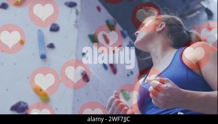 Più icone del cuore che fluttuano contro una donna caucasica che applica gesso alle mani in palestra Foto Stock