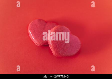 Macaron francesi a forma di cuore rosa su sfondo rosso. Concetto per San Valentino. Posiziona per testo. Foto Stock