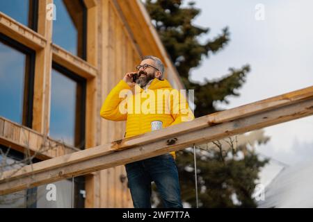 Uomo in piedi sul patio delle cabine, bevendo tè caldo, caffè e godendosi una splendida giornata invernale. Bell'uomo che trascorre un weekend invernale rilassante e senza stress Foto Stock