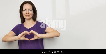 Ispira l'inclusione. Gli Zoomers simboleggiano l'amore. T-shirt viola da donna con cuore al dito. Mano che mostra il cuore. Striscione della giornata internazionale della donna 2024 Foto Stock