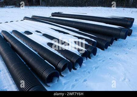 I tubi di drenaggio corrugati in plastica nera sono disposti in modo ordinato sulla superficie innevata durante l'inverno. Foto Stock