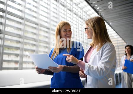 Due medici donne che discutono i risultati dei test, la diagnosi dei pazienti. attraversa il corridoio a piedi. Donne nella scienza della medicina Foto Stock