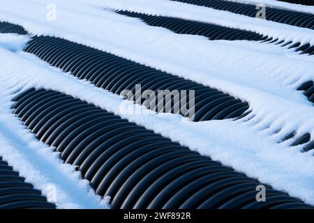 Tubi di scarico corrugati in plastica nera coperti dalla neve. Foto Stock