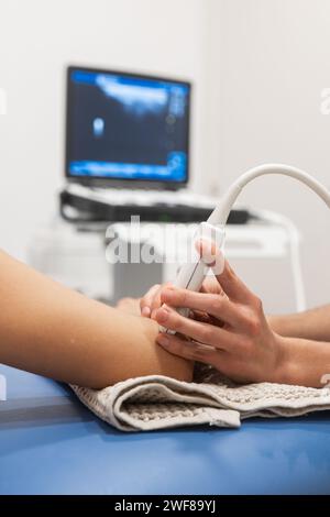 Un medico esegue un'ecografia sul braccio di un paziente con un monitor sullo sfondo Foto Stock