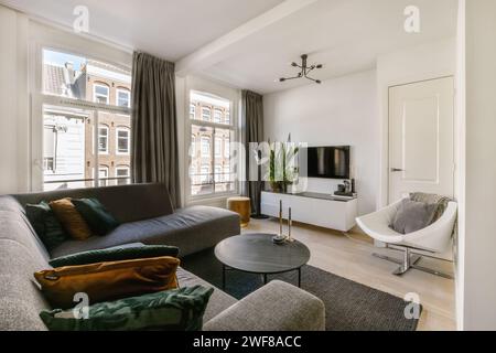 Soggiorno luminoso e moderno con grande divano, arredamento contemporaneo e grandi finestre con vista sulla città. Foto Stock