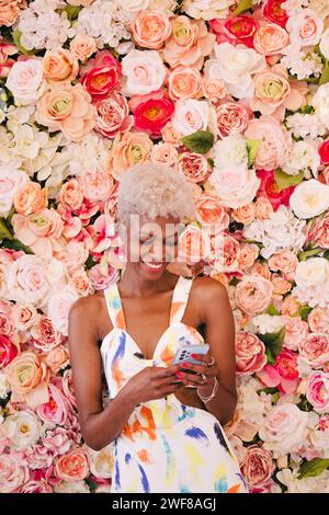 Ritratto di una giovane donna panamense con capelli biondi corti in un abito elegante. Sorride e oltre a un muro fiorito di fiori dai toni rosa Foto Stock
