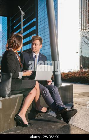 Due professionisti impegnati in una discussione con un portatile, seduti all'aperto a Madrid. Foto Stock