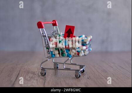 Un carrello traboccante di pillole colorate con una freccia rossa rivolta verso l'alto. Copia spazio. L'aumento del costo dei farmaci da prescrizione. Foto Stock