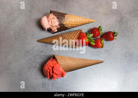 Coni per gelato con misurini di gelato alla fragola e fragole di frutta. Messa a fuoco morbida Foto Stock