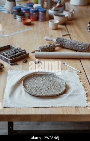 Bellissimo piatto di argilla grezza con ornamento sul tavolo in officina Foto Stock