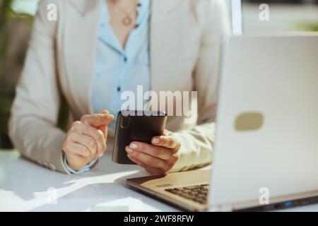 Primo piano su una donna impiegata in una tuta da lavoro leggera in un ufficio ecologico con laptop che utilizza applicazioni per smartphone. Foto Stock