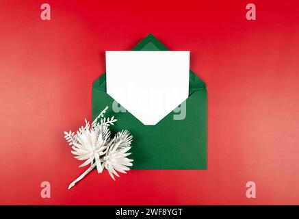 Vista dall'alto della busta verde, della scheda bianca e della diramazione invernale su sfondo rosso. Composizione per Natale e Capodanno. Foto Stock