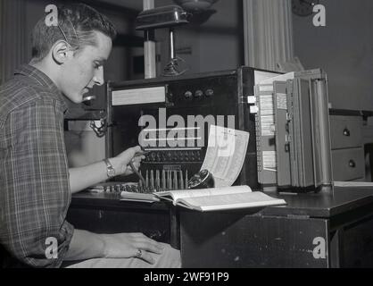 1950s, storico operatore telefonico con una Handy Phone Card, pubblicato nel gennaio 1950 con Hand Written Amendments USA, operatore di cuffie/auricolari per telegrafo, nome sulla macchina New Eng Tel & Tel, formalmente conosciuto come theTelephone & Telegraph Company, una società di telecomunicazioni fondata nel 1883. Nel marzo 1876, Alexander Graham Bell ricevette il suo primo brevetto statunitense per il telefono e diversi giorni dopo fu fatto un discorso chiaro nel laboratorio di Boston di Bell. Foto Stock