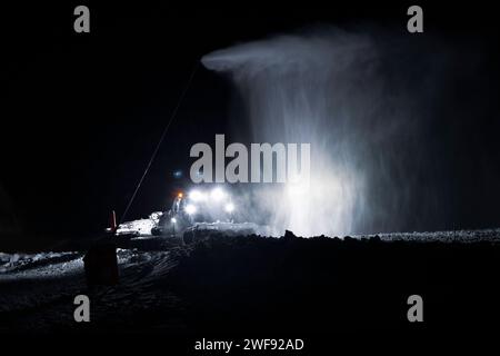 Un rastrello che opera di notte sotto un cannone innevato in Val-Cenis, una stazione sciistica delle Alpi francesi Foto Stock