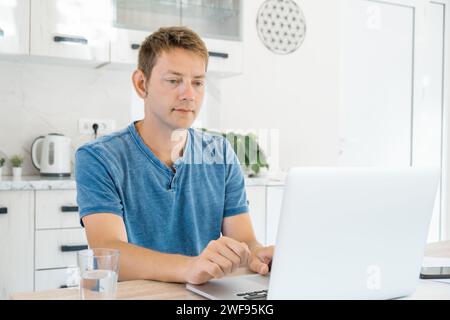 Giovane uomo attraente che lavora su un portatile online a casa, usando Internet. Freelance maschio che utilizza il computer per lavori a distanza. Processo remoto. Tecnologia moderna Foto Stock