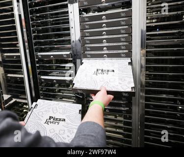 PRODUZIONE - 07 dicembre 2023, Schleswig-Holstein, Grömitz: Un dipendente sente i vani frigoriferi di un distributore automatico di pizza in un chiosco di distributori automatici sul lungomare. Foto: Christian Charisius/dpa Foto Stock