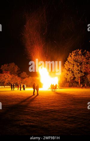 Gruppo di individui riuniti intorno a un grande falò, illuminando il cielo notturno, in mezzo a un vasto campo aperto Foto Stock