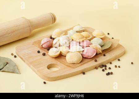 Tavola di legno di gnocchi crudi colorati con pepe e foglie di alloro su sfondo giallo Foto Stock