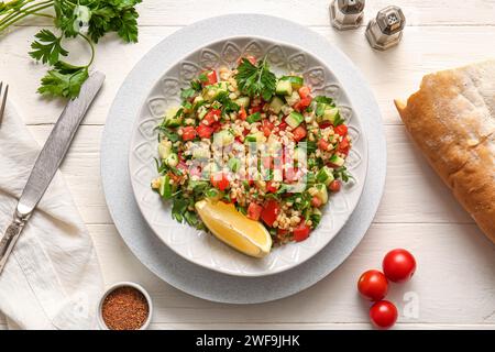 Piatto con deliziosa insalata tabbouleh e pane su sfondo di legno chiaro Foto Stock