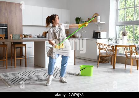 Bella giovane donna che si diverte con lo spazzolone in cucina moderna Foto Stock