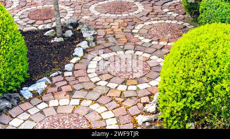 Pavimentazione circolare di un sentiero vicino alla casa e nel giardino. Una variante originale di pietre per pavimentazione per i sentieri del giardino. Passerella in granito rosso e bianco Foto Stock