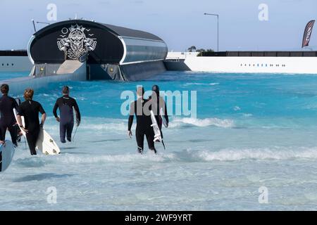 Le persone camminano in acqua con le tavole da surf sotto le braccia a Urbnsurf, la prima piscina a onde commerciale dell'Australia a Melbourne Foto Stock