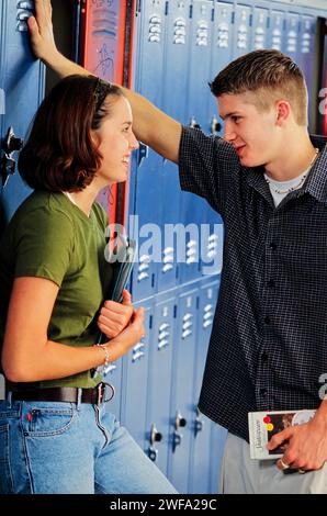 Due studenti delle scuole superiori stanno facendo una chiacchierata amichevole accanto ai loro armadietti aperti nel corridoio durante una pausa tra le lezioni. Foto Stock