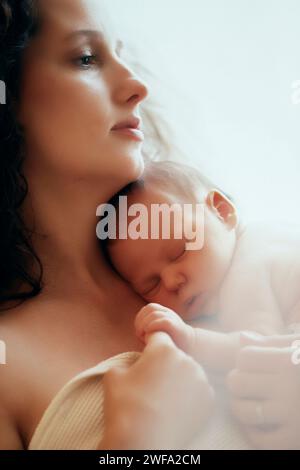 Una donna culla dolcemente un neonato tra le braccia, creando un delicato momento di amore e cura. Foto Stock