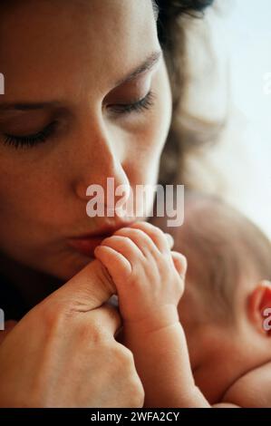 Madre poco attraente che bacia delicatamente la mano del suo neonato Foto Stock