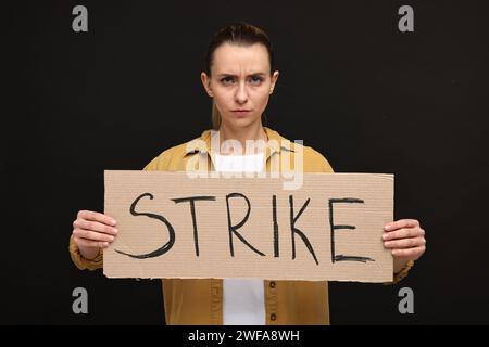 Donna arrabbiata con striscione in cartone con la parola Strike su sfondo nero Foto Stock