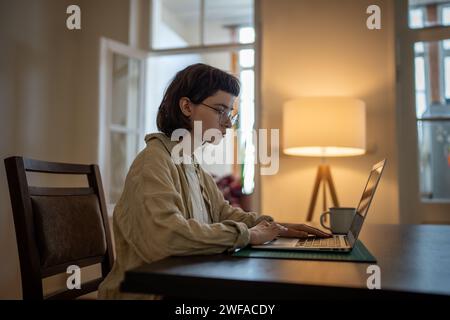 Una ragazza freelance concentrata che lavora su un laptop si trova a casa sul posto di lavoro, impara la lingua inglese online Foto Stock