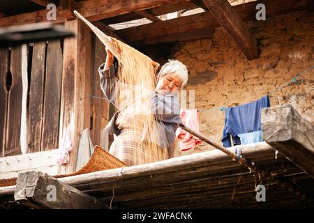 La donna bhutanese sta versando riso su un balcone di legno per asciugarsi durante il raccolto, Trongsa, Bhutan, Asia Foto Stock