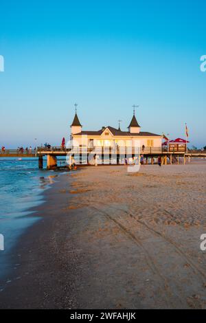 Persone che passeggiano su un molo con edifici al tramonto, cielo limpido, blu, senza nuvole, molo Ahlbeck all'ultima luce del sole, vista dalla spiaggia occidentale Foto Stock