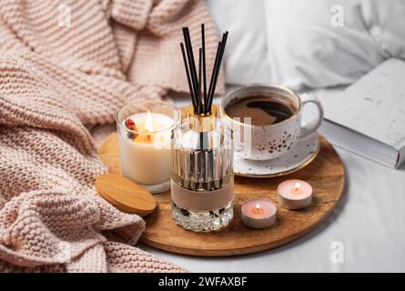 Bastoncini di bambù in bottiglia con candele profumate e una tazza di caffè sul letto. Atmosfera accogliente. Foto Stock