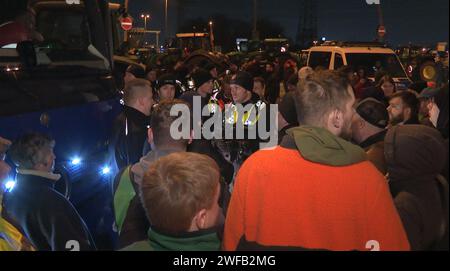 Amburgo, Germania. 30 gennaio 2024. Gli agenti di polizia discutono con gli agricoltori nel loro blocco in un incrocio con accesso al porto a sud di Amburgo. Le proteste degli agricoltori sono proseguite fino a martedì sera. Gli agricoltori continuano a paralizzare le principali arterie di traffico intorno al porto di Amburgo. L'azione ha conseguenze di vasta portata per i fornitori e comporta notevoli ostacoli al traffico. Crediti: Steven Hutchings/dpa/Alamy Live News Foto Stock