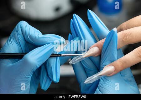 Manicurista con una spazzola fine per rifinire un'unghia di bordo durante la manicure. Foto Stock