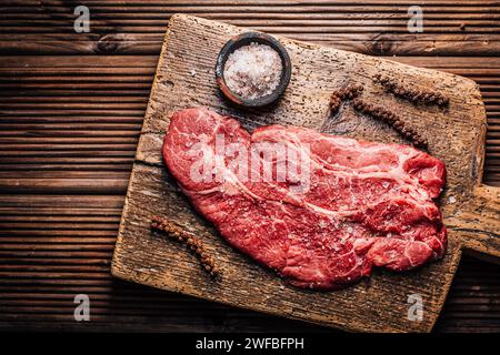 Bistecca di manzo crudo di manzo manzo condita con sale e pepe su tagliere di legno Foto Stock