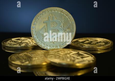 Fotografia di Bitcoin dorati isolati su sfondo nero riflettente, circondati da una pila di monete. Criptovaluta. Valuta digitale decentrata. Foto Stock