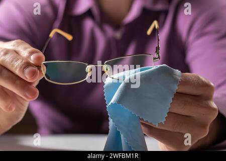 Pulizia degli occhiali. Un uomo gli asciuga gli occhiali con un panno. Messa a fuoco selettiva Foto Stock